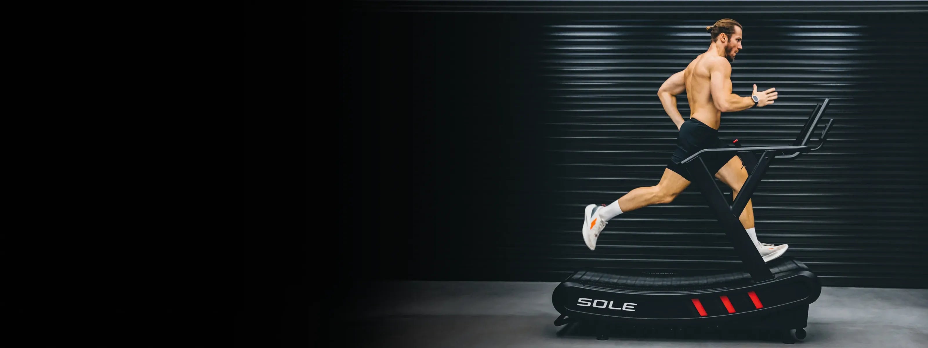 A runner on the SOLE C80 curved manual treadmill on a dark studio stage