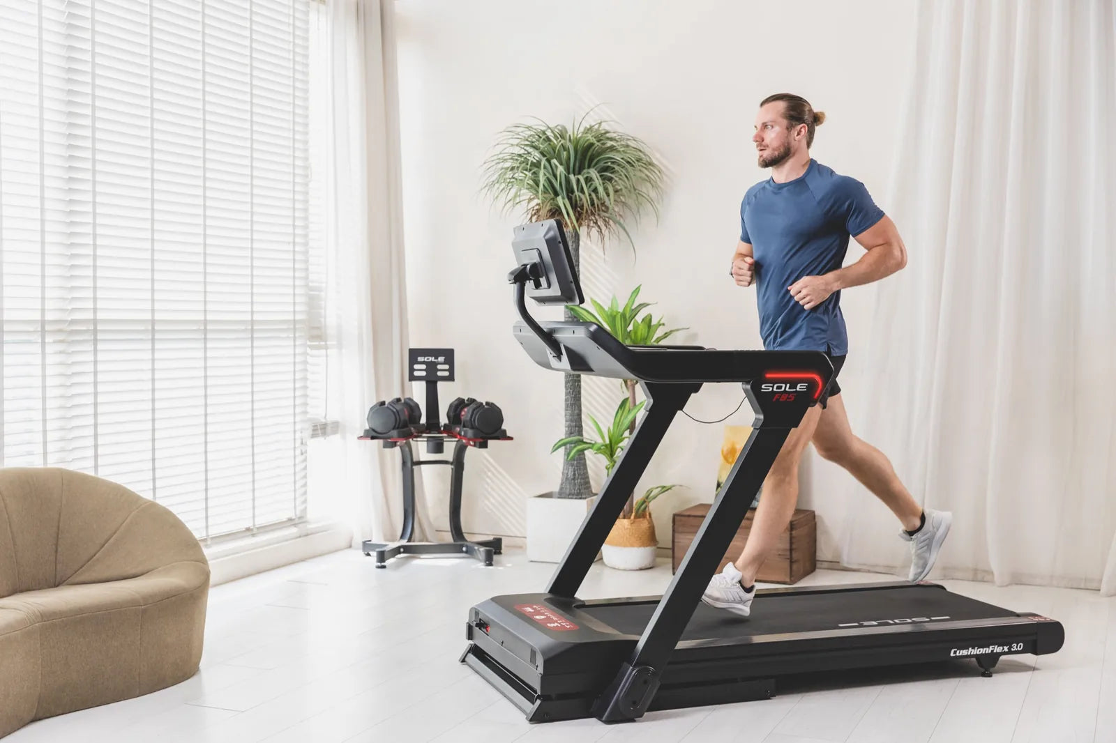 A man running on a SOLE F85 CushionFlex 3.0 treadmill in a bright living room.